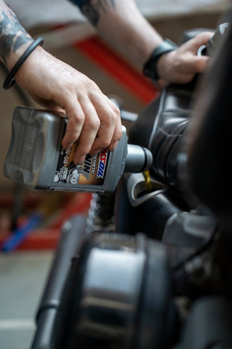 Close-up of a mechanic pouring engine oil into a motorcycle inside a garage.